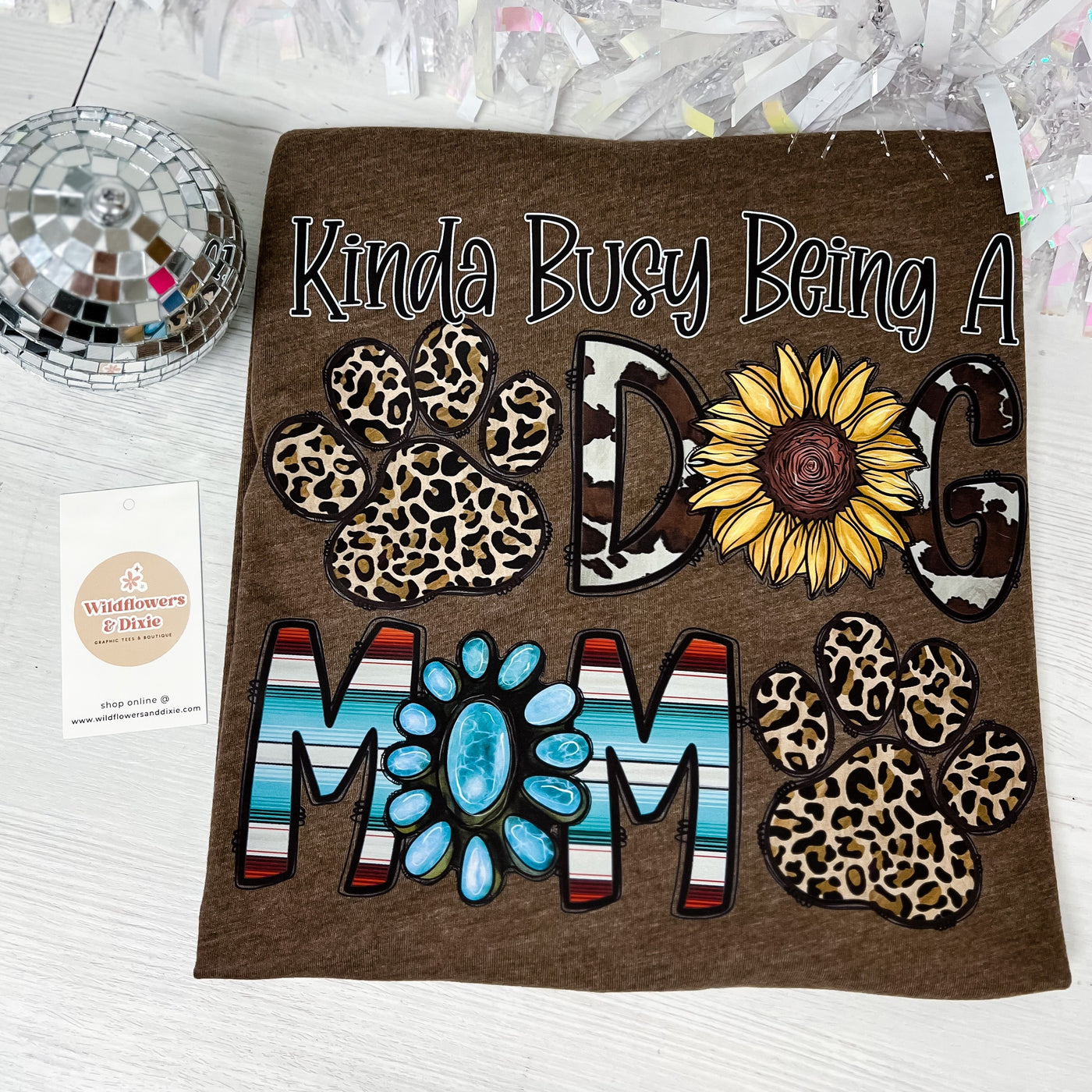 Kinda Busy Being a Dog Mom graphic t-shirt with leopard and cow print font, sunflowers, and other country/western elements