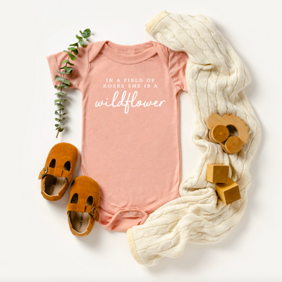 Super soft infant bodysuit featuring the phrase "In a Field of Roses, She is a Wildflower." The perfect baby shower gift idea for mommy-to-be, Mother's Day outfit, birthday party, or every day!