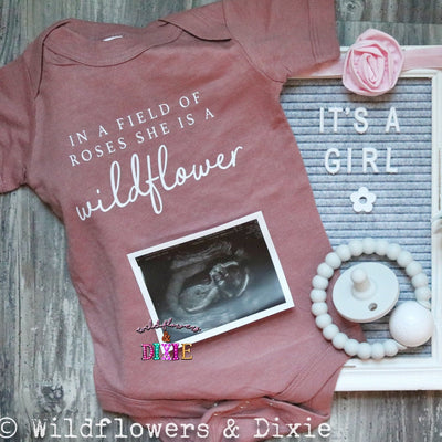 Super soft infant bodysuit featuring the phrase "In a Field of Roses, She is a Wildflower." The perfect baby shower gift idea for mommy-to-be, Mother's Day outfit, birthday party, or every day! Shown here as a gender reveal announcement.